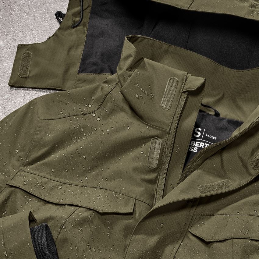 Close-up of an olive-green rain jacket with water droplets, a high collar, zip fastening and adjustable hook-and-loop closures.
